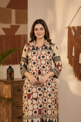 A woman modeling a long-sleeved kurta with a geometric circle and triangle pattern in beige, brown, and black, paired with dark brown pants in a styled bohemian room setting.