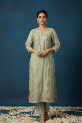 Woman wearing a light green traditional outfit with floral patterns on a dark blue background.